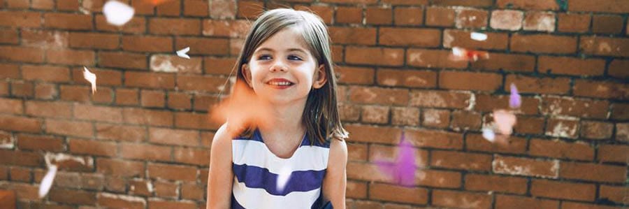 Petite fille souriante près d'un mur de briques